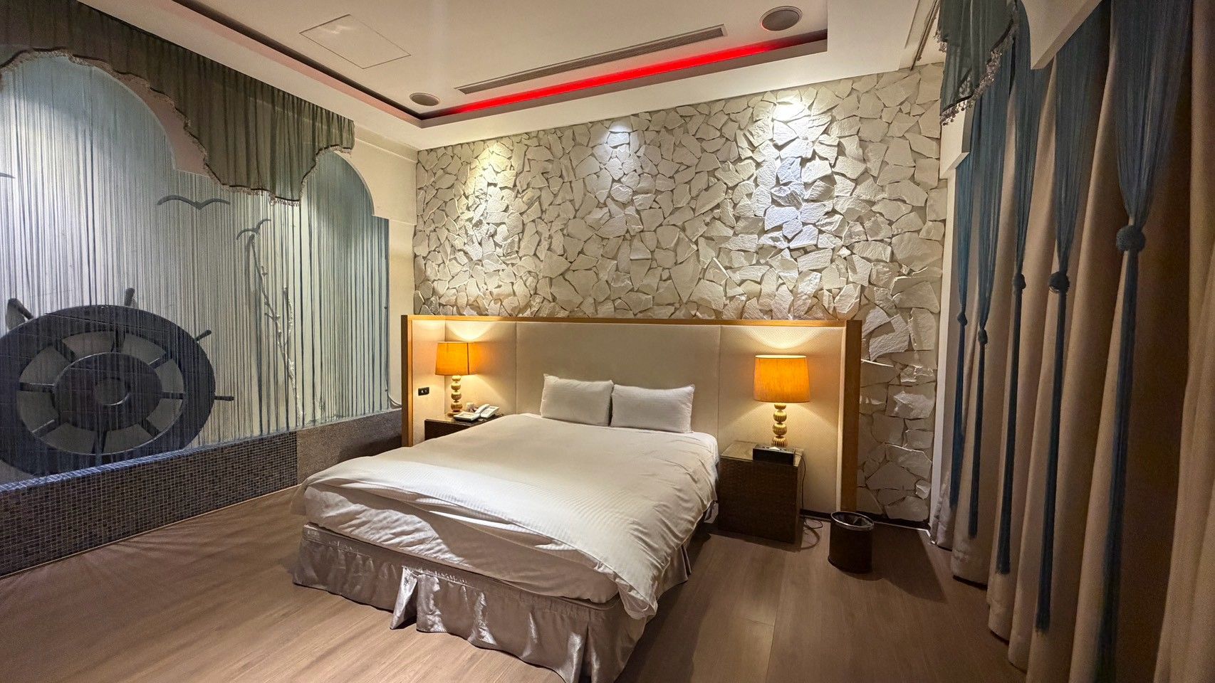 A hotel room with a large bed, two bedside lamps, a decorative wall, and a curtain.