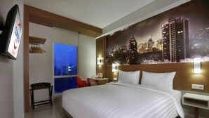 Une chambre d’hôtel avec un grand lit, une fresque représentant un paysage urbain, un téléviseur et une fenêtre donnant sur la ville de nuit.
