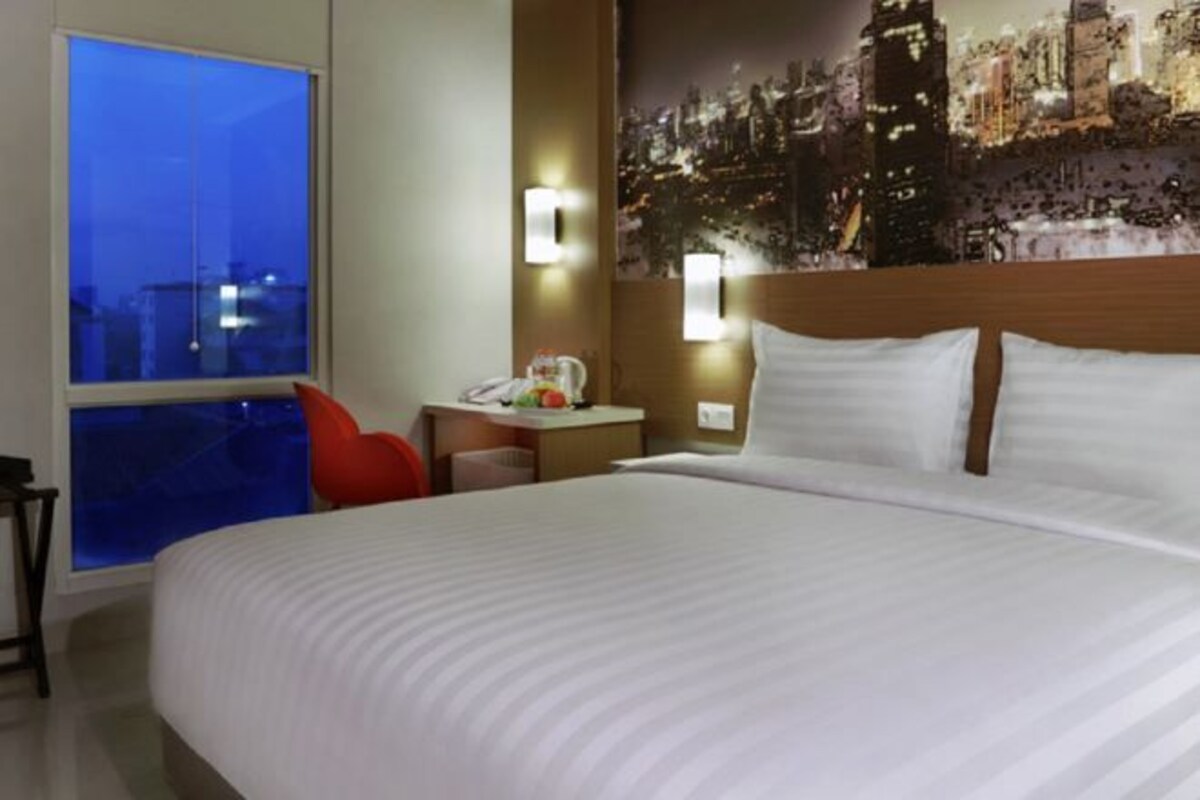Hotelkamer met een groot bed, een bureau met stoel, een nachtkastje en uitzicht op de stad.
