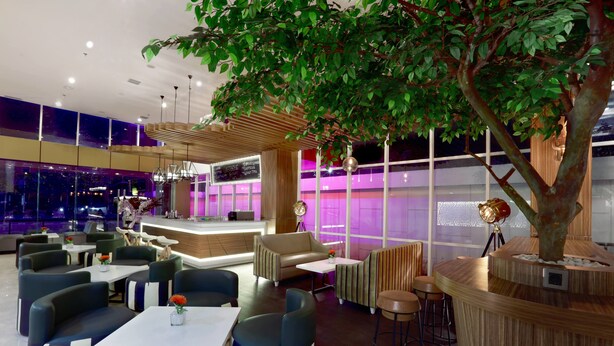 Un espace de détente moderne, aménagé avec des sièges confortables, un comptoir d’accueil et un grand arbre servant d’élément décoratif central.