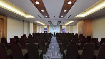 A conference room with rows of chairs facing a podium, a banner with hotel branding, and wooden paneling on the ceiling.