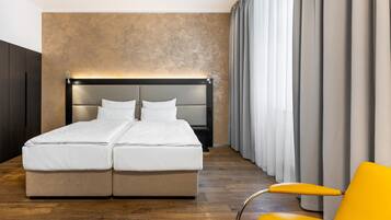 Una cama doble con cabecera, un sillón amarillo y un ventanal con cortinas.