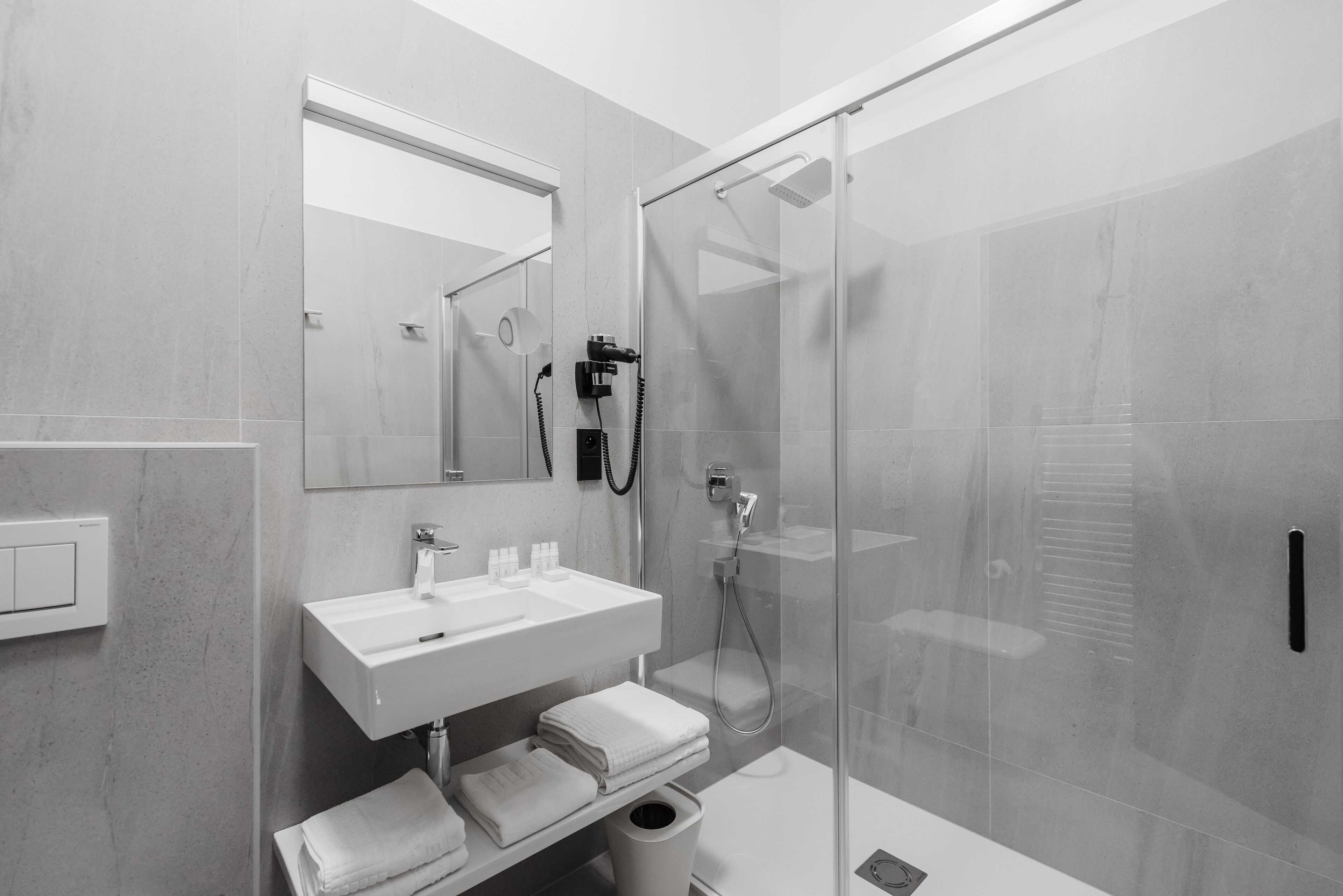 Un baño moderno con ducha envuelta en vidrio, un lavamanos blanco y un espejo encima.