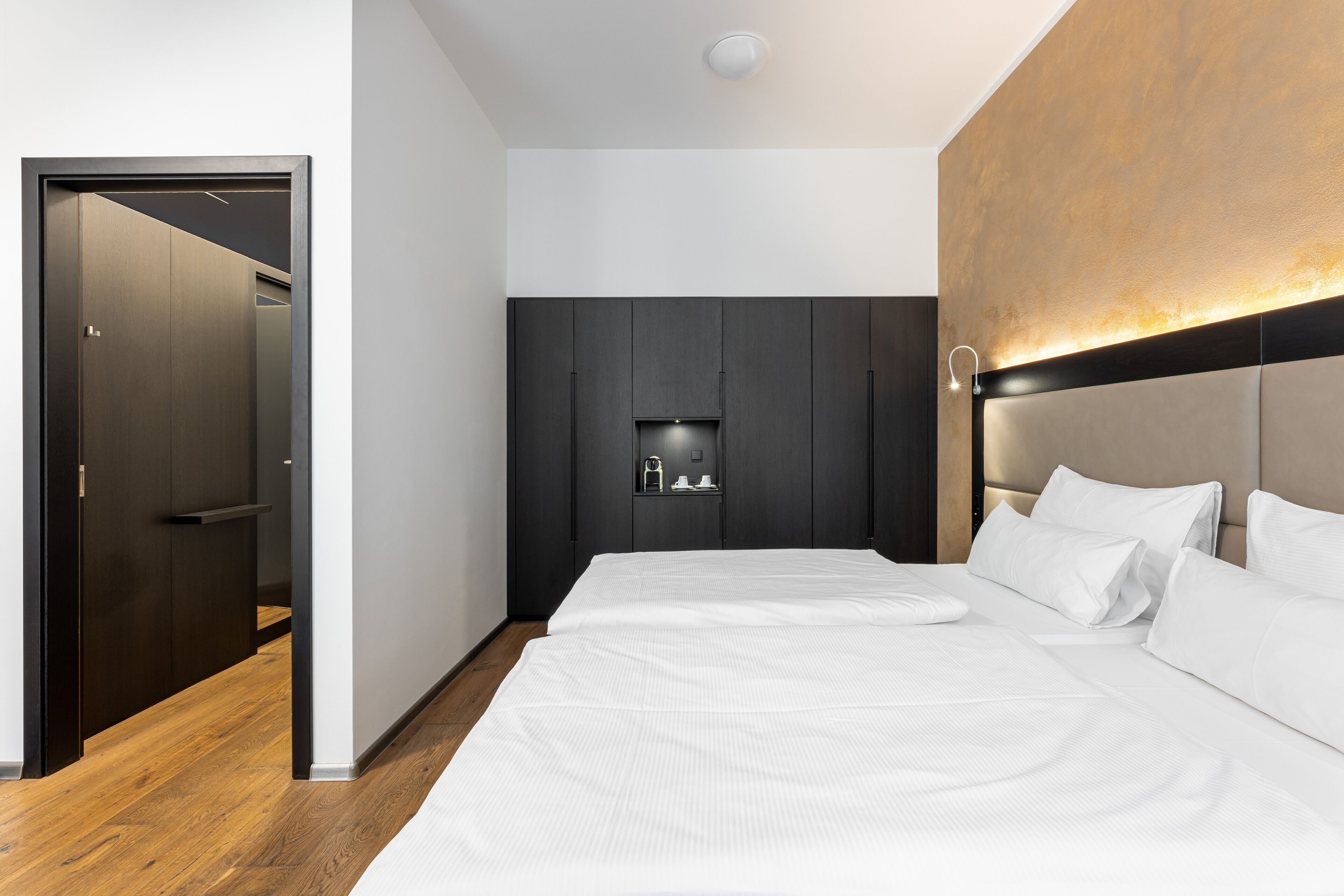 A modern bedroom with a large bed, dark wooden wardrobe, and a built-in shelf with a light.