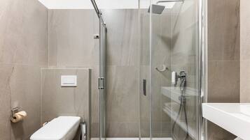 A modern bathroom with a glass-enclosed shower, a toilet, and a sink.