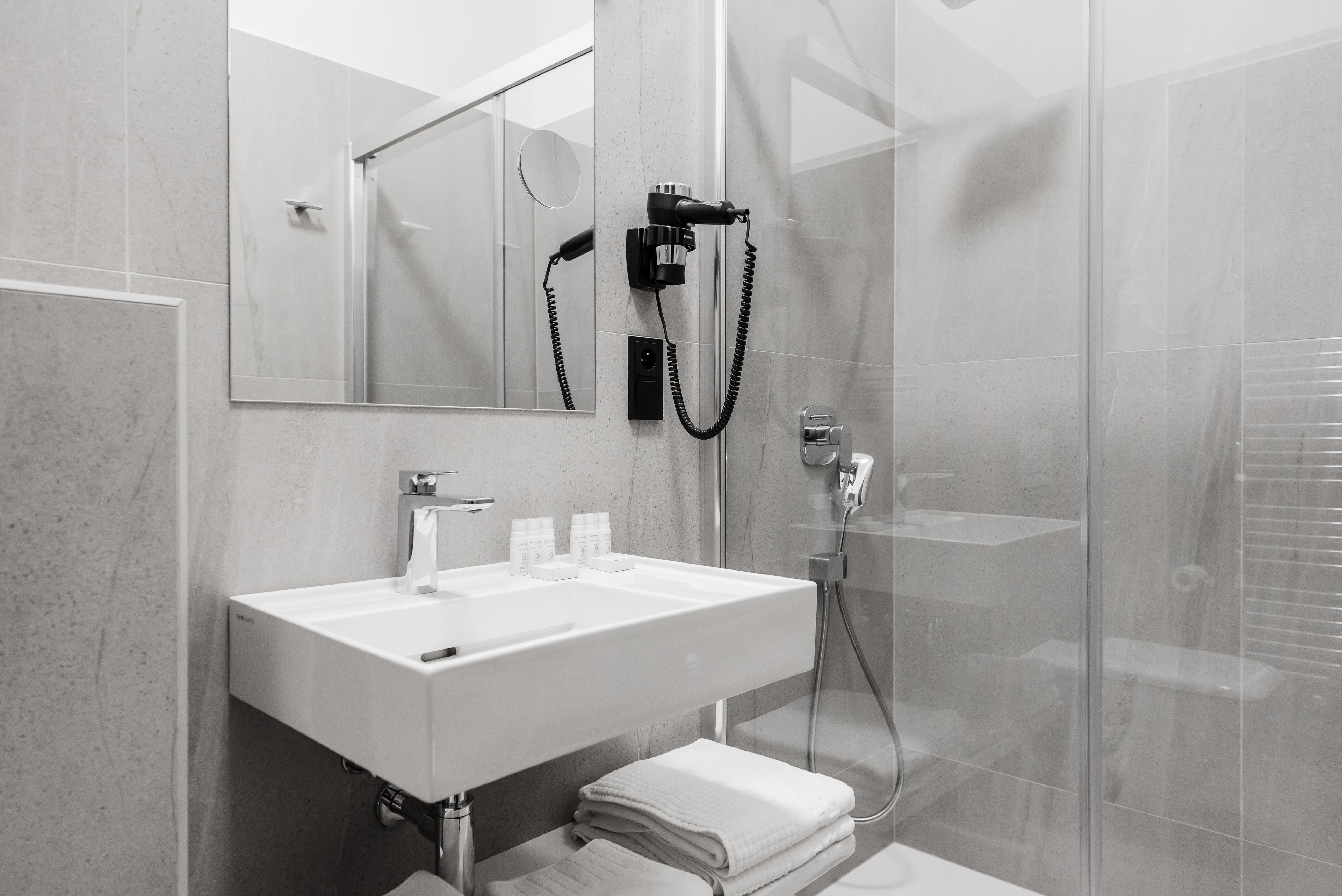 A modern bathroom with a white sink, mirror, and glass shower enclosure.