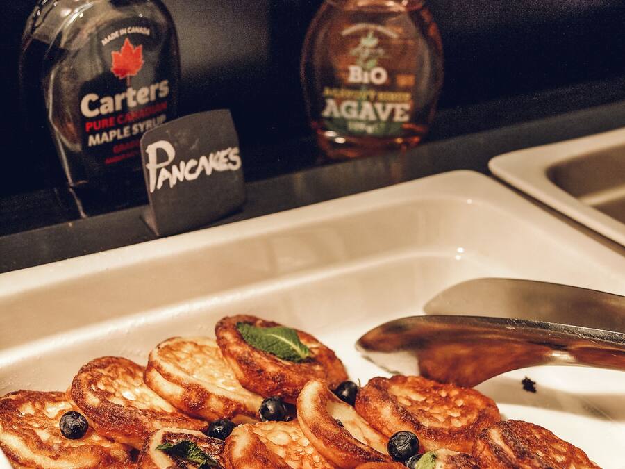 A breakfast tray with pancakes, blueberries, and a sign indicating the availability of maple syrup and agave syrup.