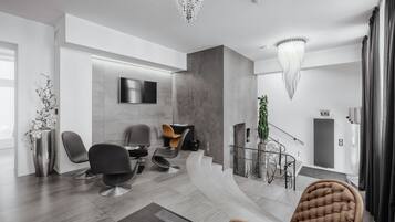 A modern interior with a curved seating area, a mounted TV, and a staircase leading to an upper level.