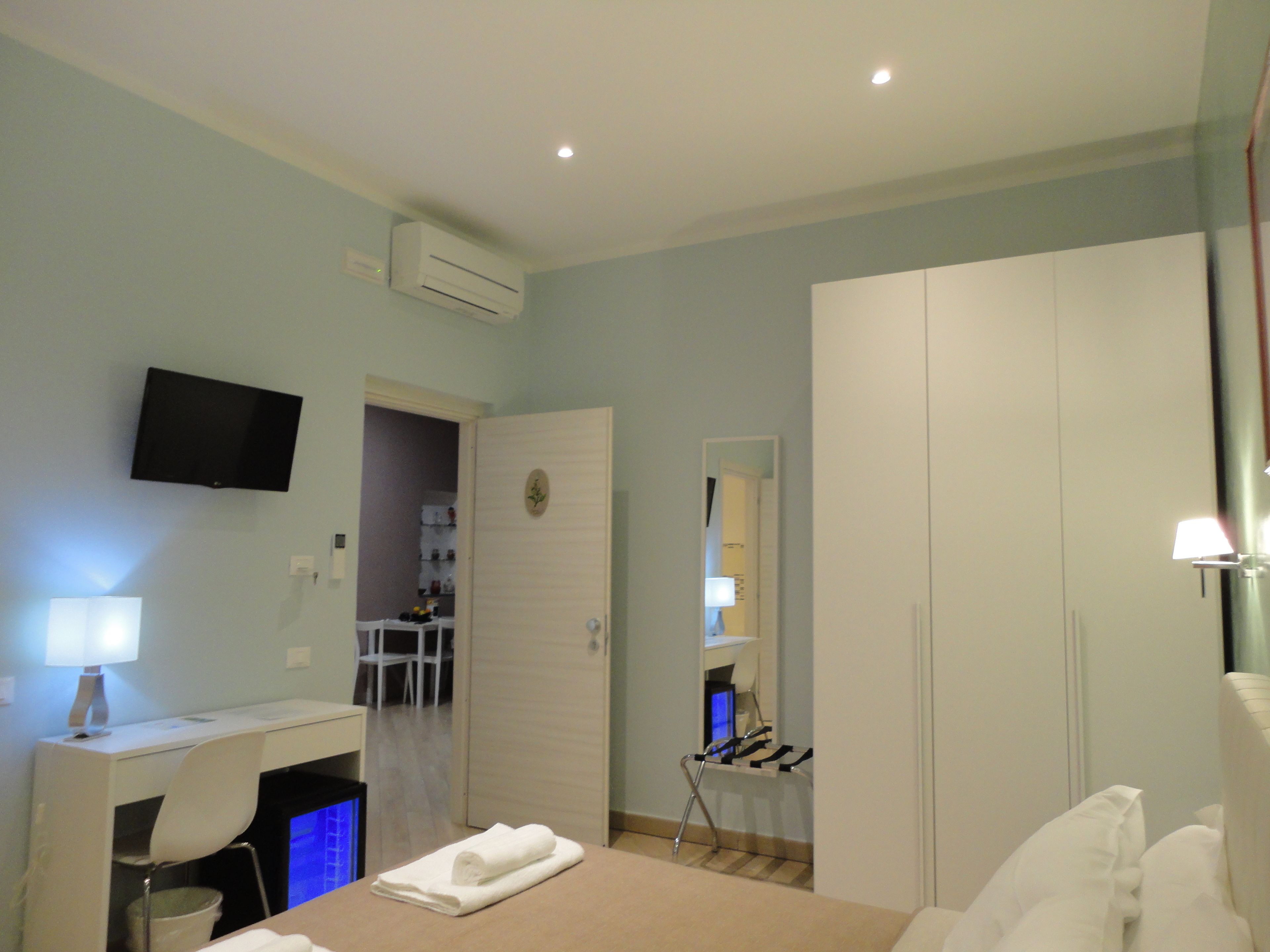 Ein Schlafzimmer mit Bett, Schreibtisch, Stuhl, Fernseher, Kleiderschrank und einem durch eine offene Tür einsehbaren Badezimmer.