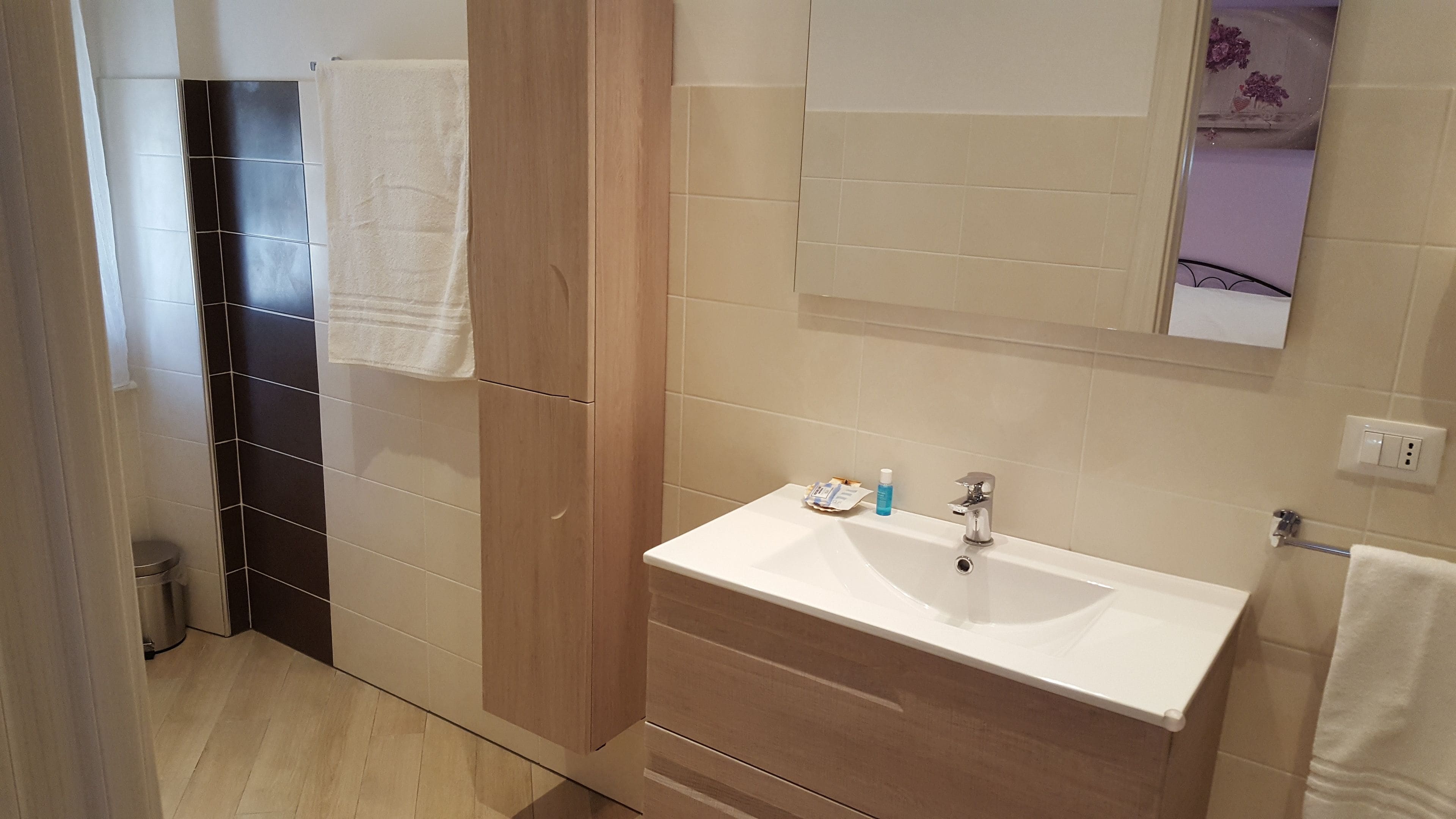 A modern bathroom with a white sink, wooden vanity, and a mirror above the sink.