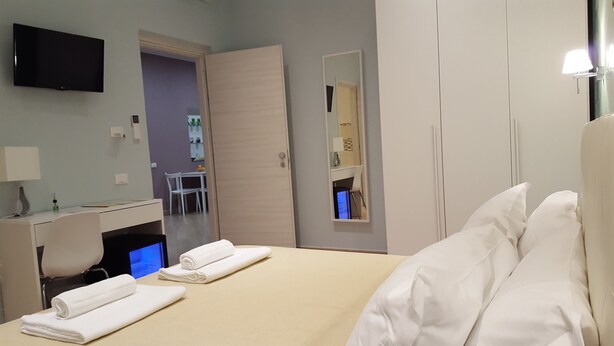 Una habitación de hotel con cama, escritorio, silla, televisión y espejo.