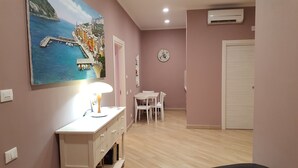 Una habitación con escritorio, silla y una mesa de comedor con sillas. Hay un cuadro en la pared, un reloj y un equipo de aire acondicionado.