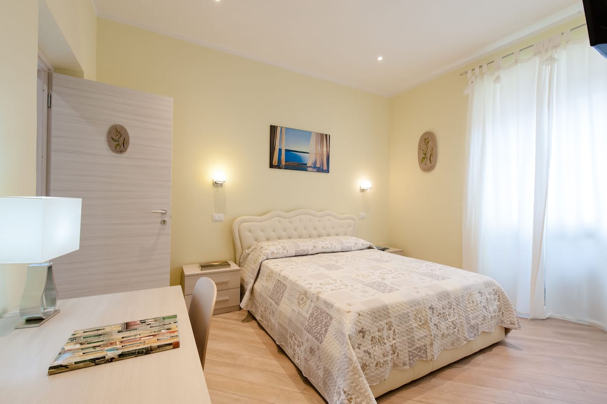 A bedroom with a bed, bedside table, lamp, and a painting on the wall.