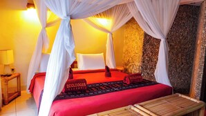 Habitación con cama bajo un dosel, pared de piedra y colcha roja con almohadones 'Ecolodges Indonesia'.