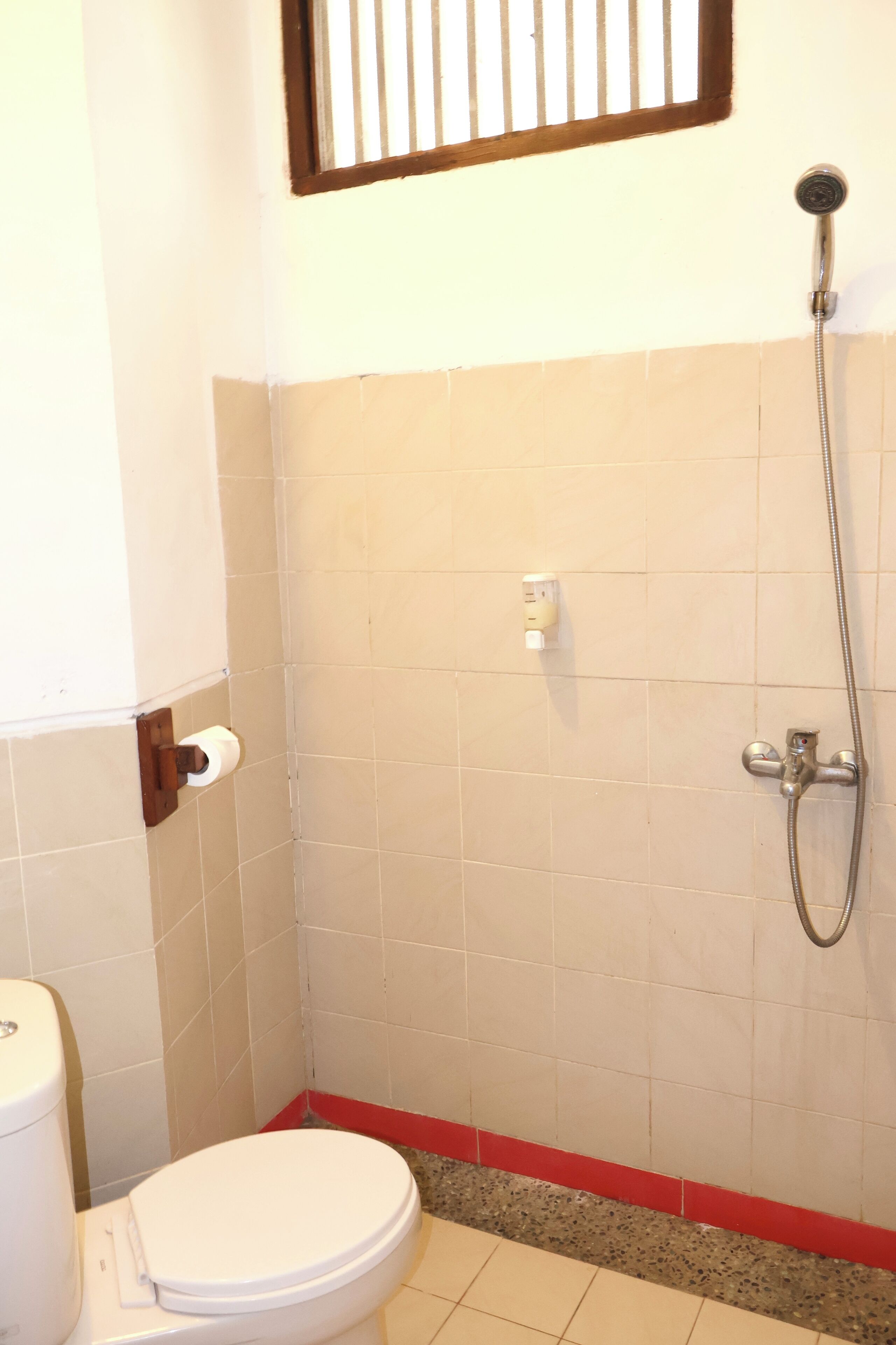 Une petite salle de bain avec des toilettes, une douche et une fenêtre.