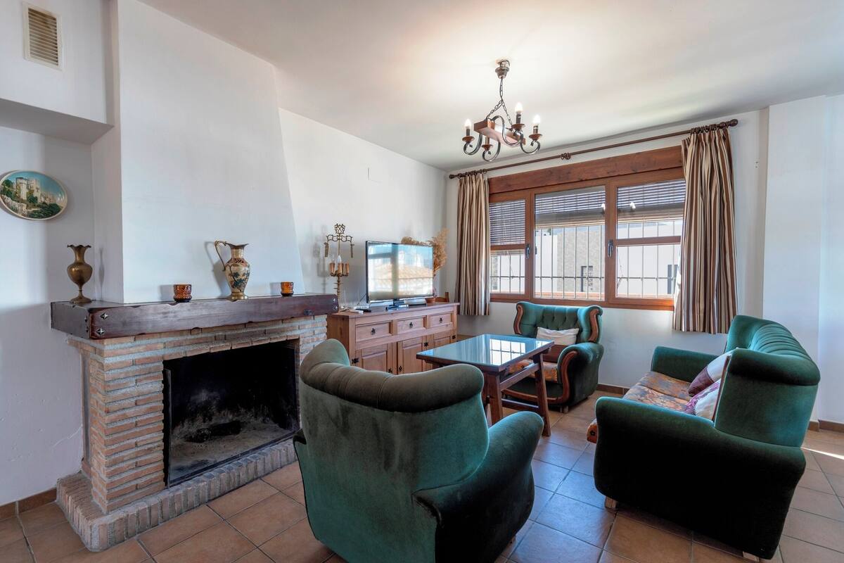 A living room with a brick fireplace, green armchairs, a wooden coffee table, and a television.