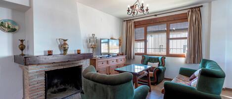 A living room with a brick fireplace, green armchairs, a wooden coffee table, and a television.