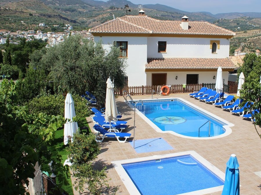 Uma área de piscina com espreguiçadeiras, um boi de salva-vidas e um edifício com telhado de azulejos.