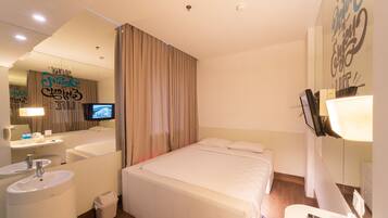 Habitación de hotel con cama, baño con lavamanos y espejo, televisión y una pared con texto motivacional.