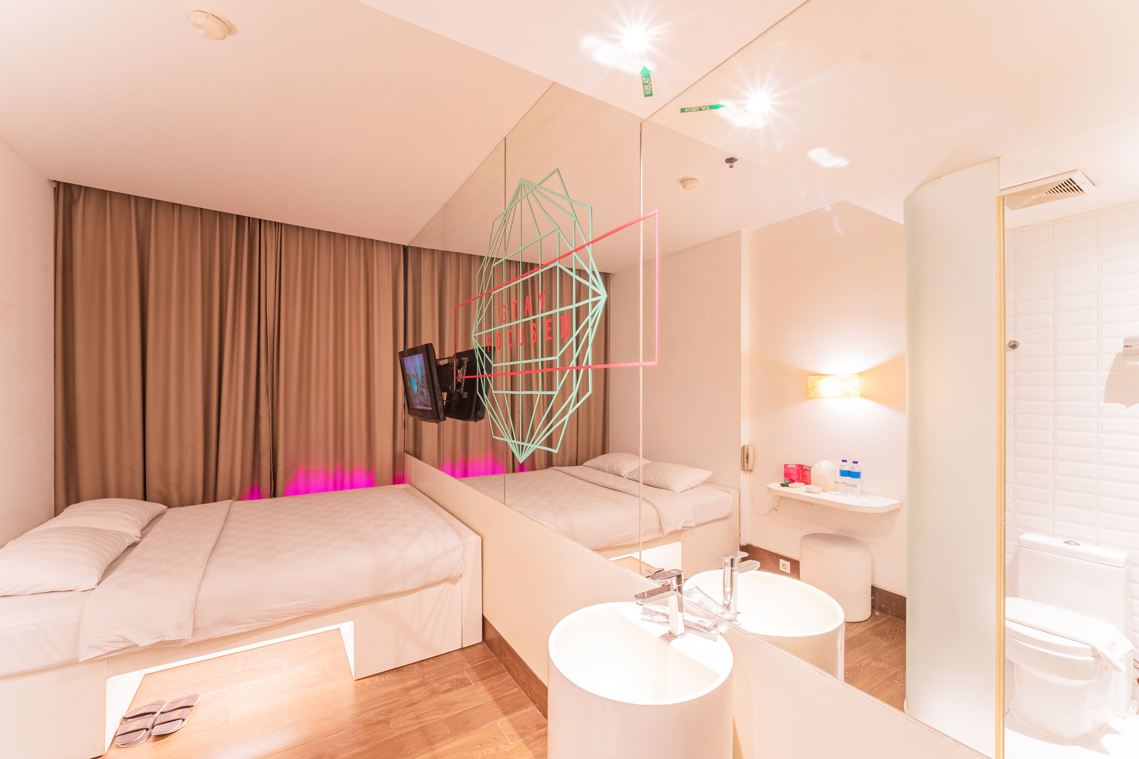 A hotel room with two beds, a TV, a bathroom with a sink and toilet, and a mirror.