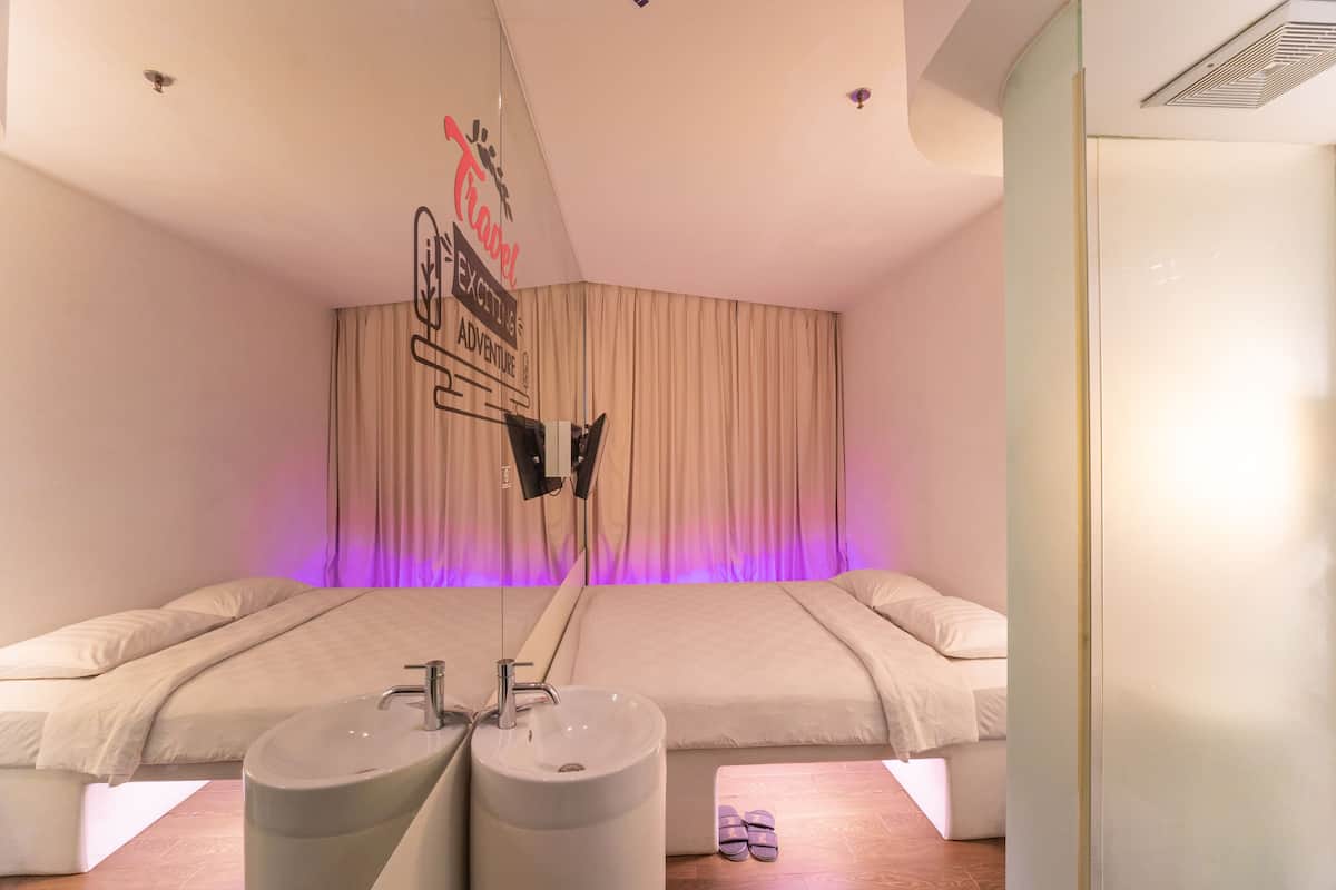 A modern hotel room with two beds, a large window with curtains, a bedside table with a lamp, and a wall-mounted TV.