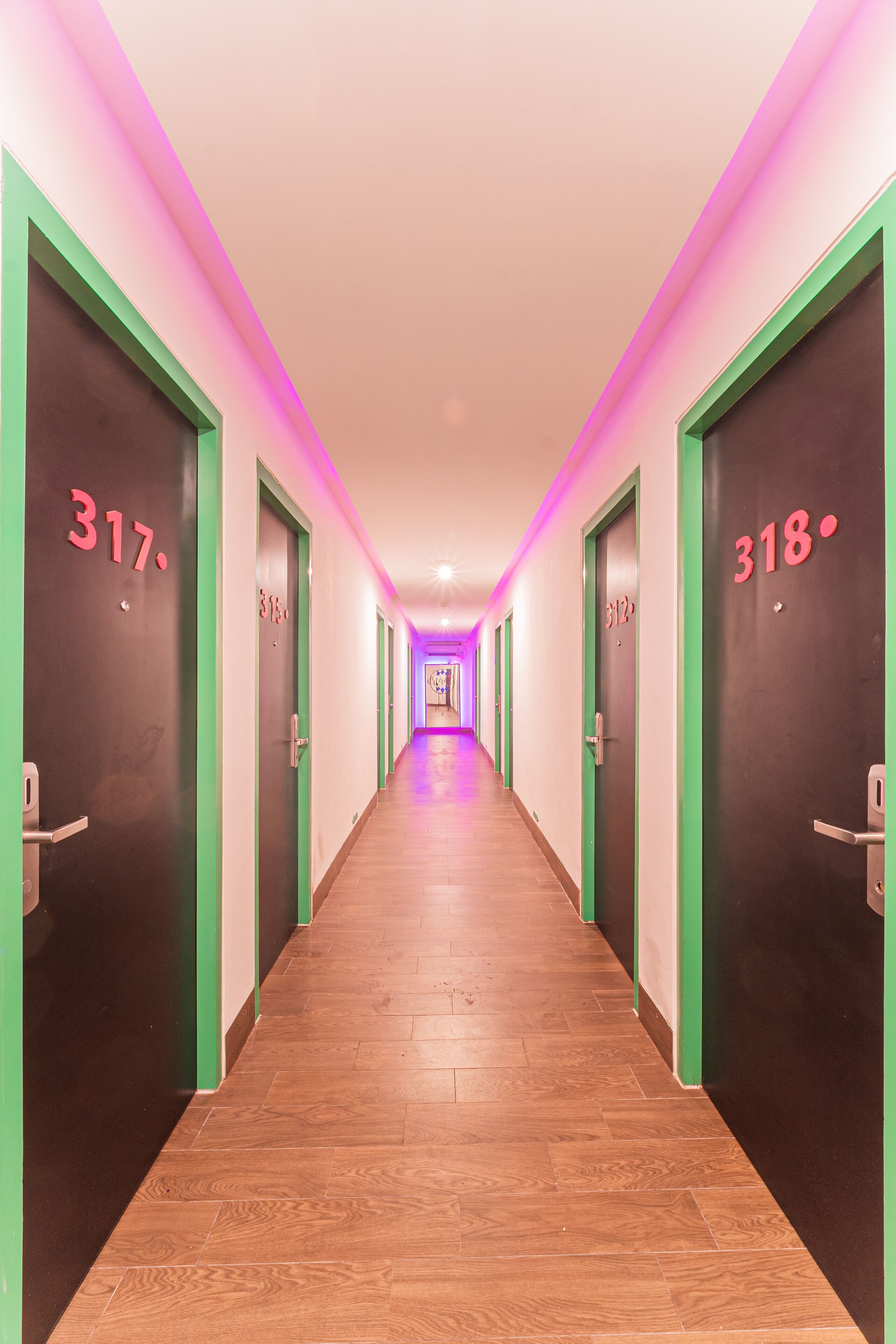 Pasillo de hotel con puertas numeradas 317 y 318, suelo de madera e iluminación rosada.