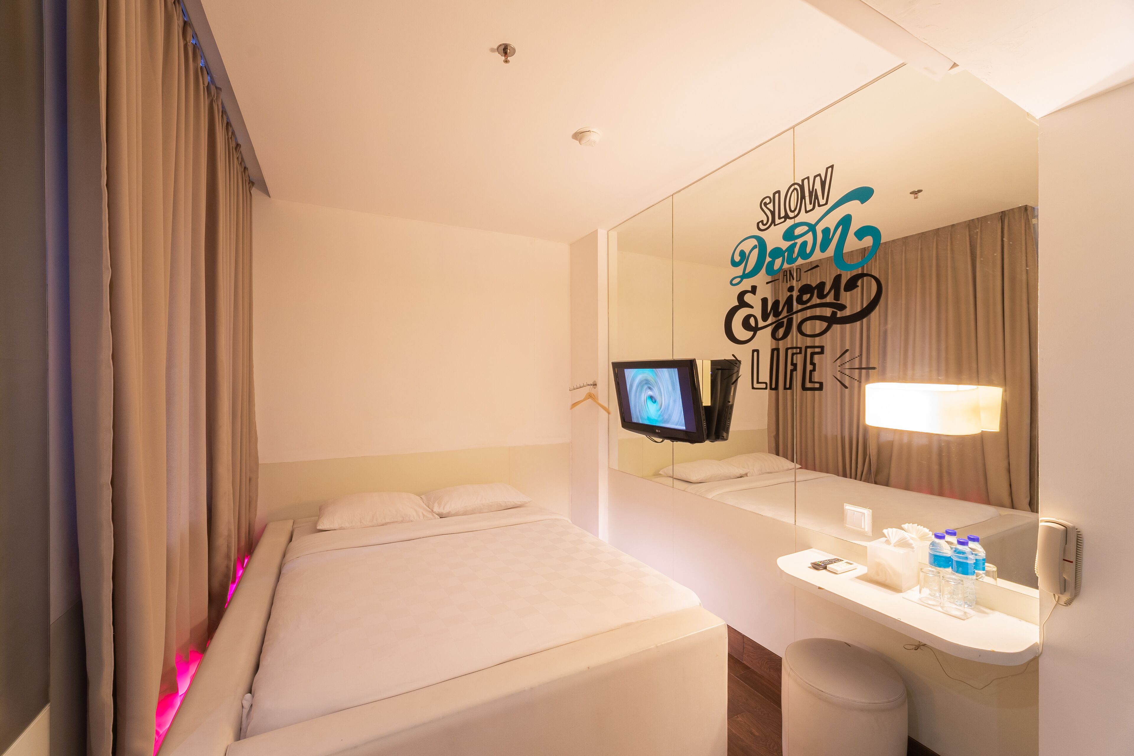 Hotelkamer met een bed, nachtkastje met televisie, spiegel en muur met een motiverende quote.
