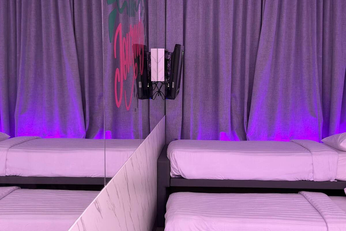 A room with two beds, purple curtains, and a mounted camera.
