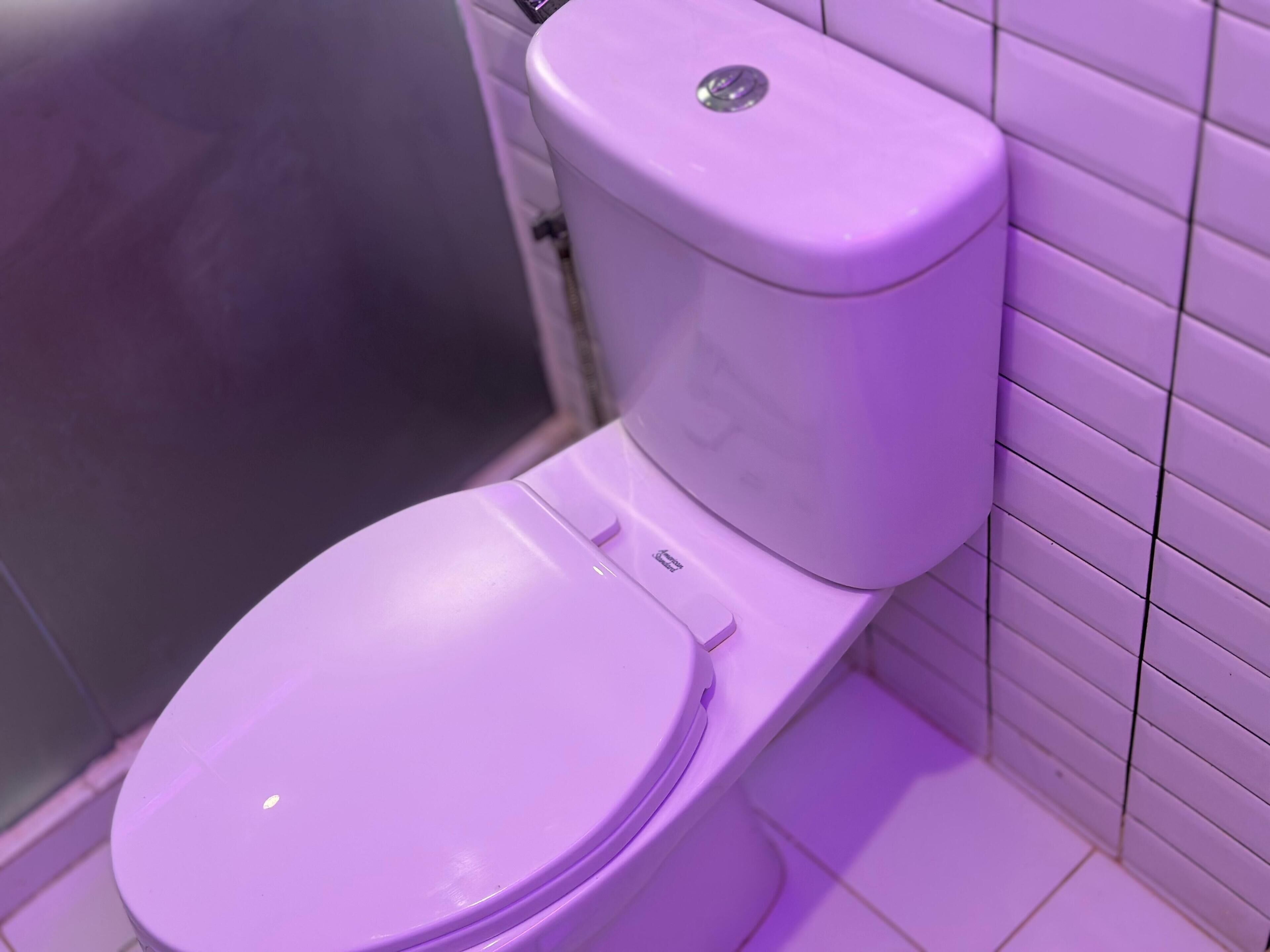 A toilet with a lid and a flush handle in a bathroom with tiled walls.