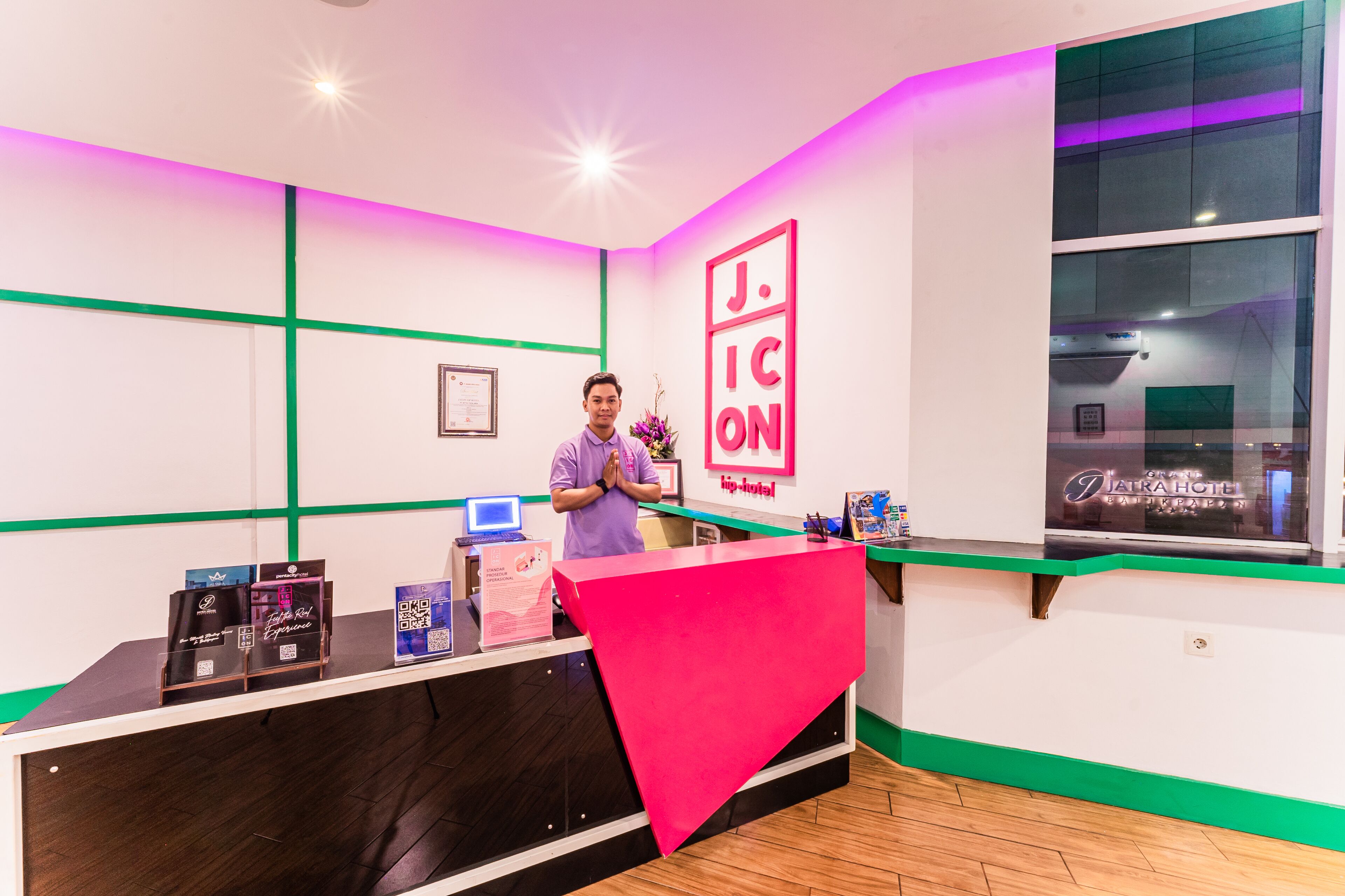 A reception desk with a pink cover, a framed certificate on the wall, and a window with a view of a building.