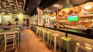 Eine Bar mit Sitzgelegenheiten, einer Theke mit Flaschen und einem Fernsehbildschirm, der ein Sportspiel zeigt.