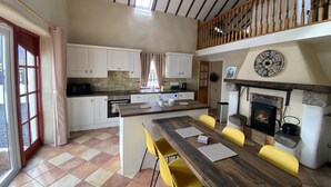 A spacious kitchen with white cabinets, a wooden island, and a stone fireplace.