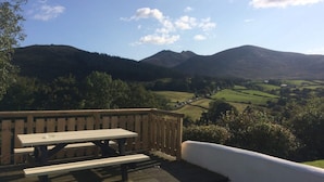 A wooden deck with picnic tables overlooking a valley with mountains in the background.