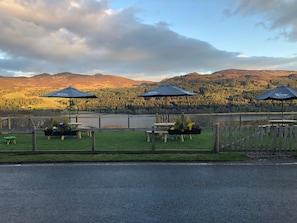 Une terrasse au bord du lac, dotée de sièges et de parasols, offrant une vue sur un paysage boisé.