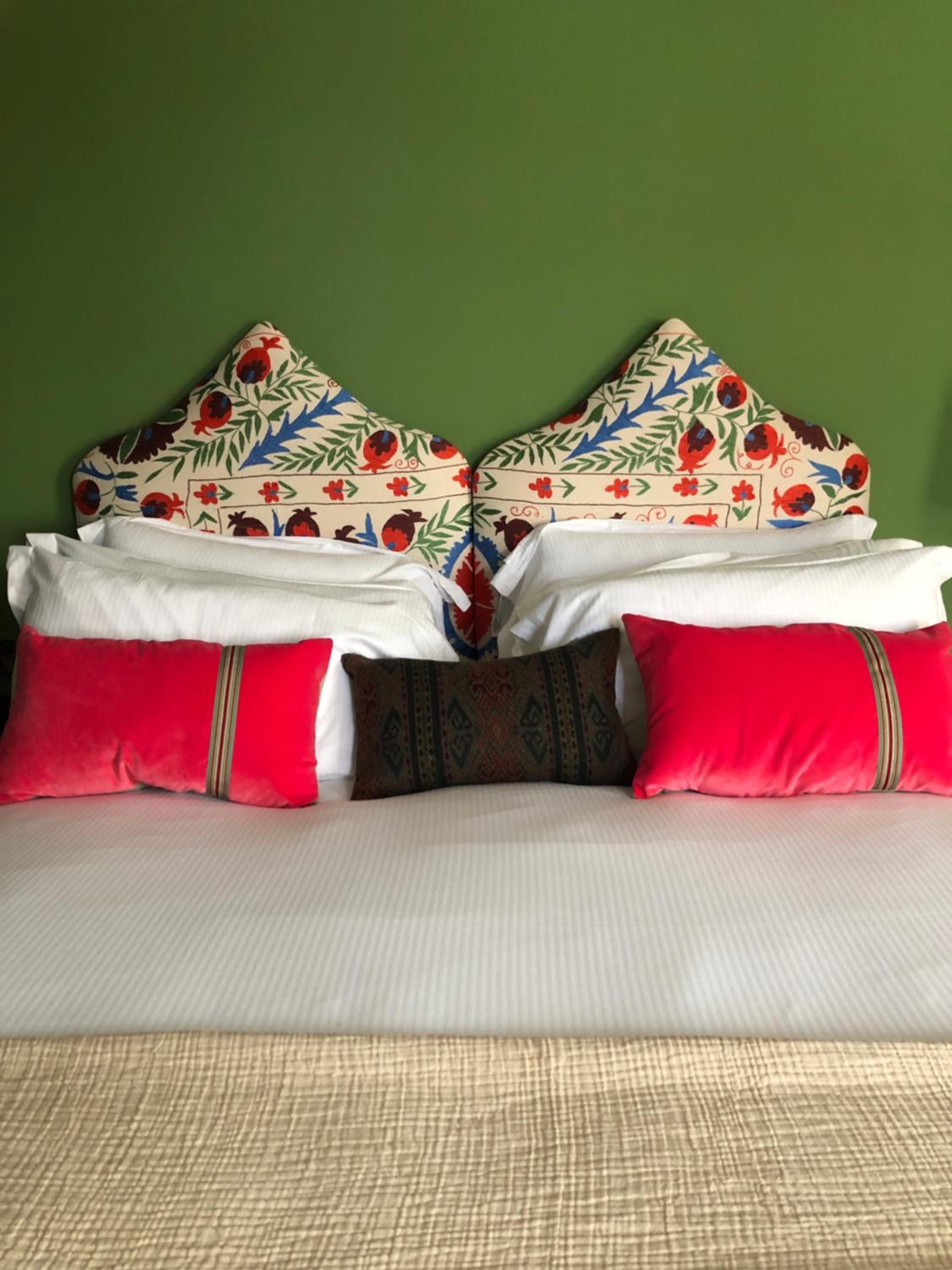 A bed with white bedding, two red pillows, and decorative pillows with floral patterns.