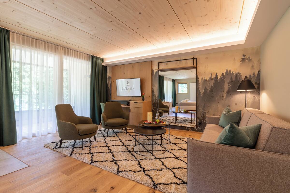 Ein modernes Wohnzimmer mit Holzböden, einer Couch, zwei Sesseln, einem Couchtisch und einem großen Spiegel an der Wand.