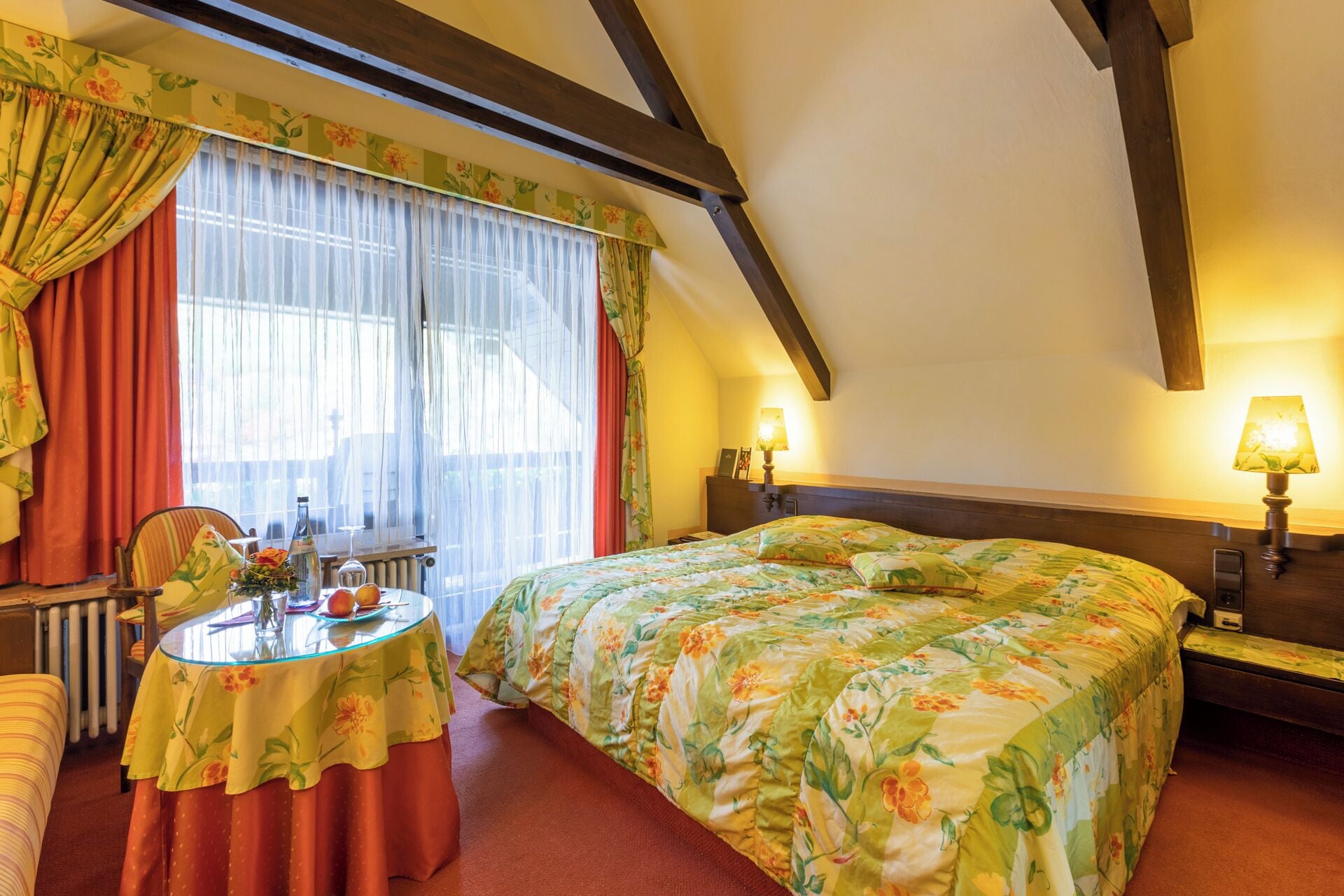 A cozy bedroom with a bed, a bedside table, a lamp, a chair, and a window with curtains.