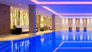 A modern indoor swimming pool with a geometric design, surrounded by stone walls and glass panels.