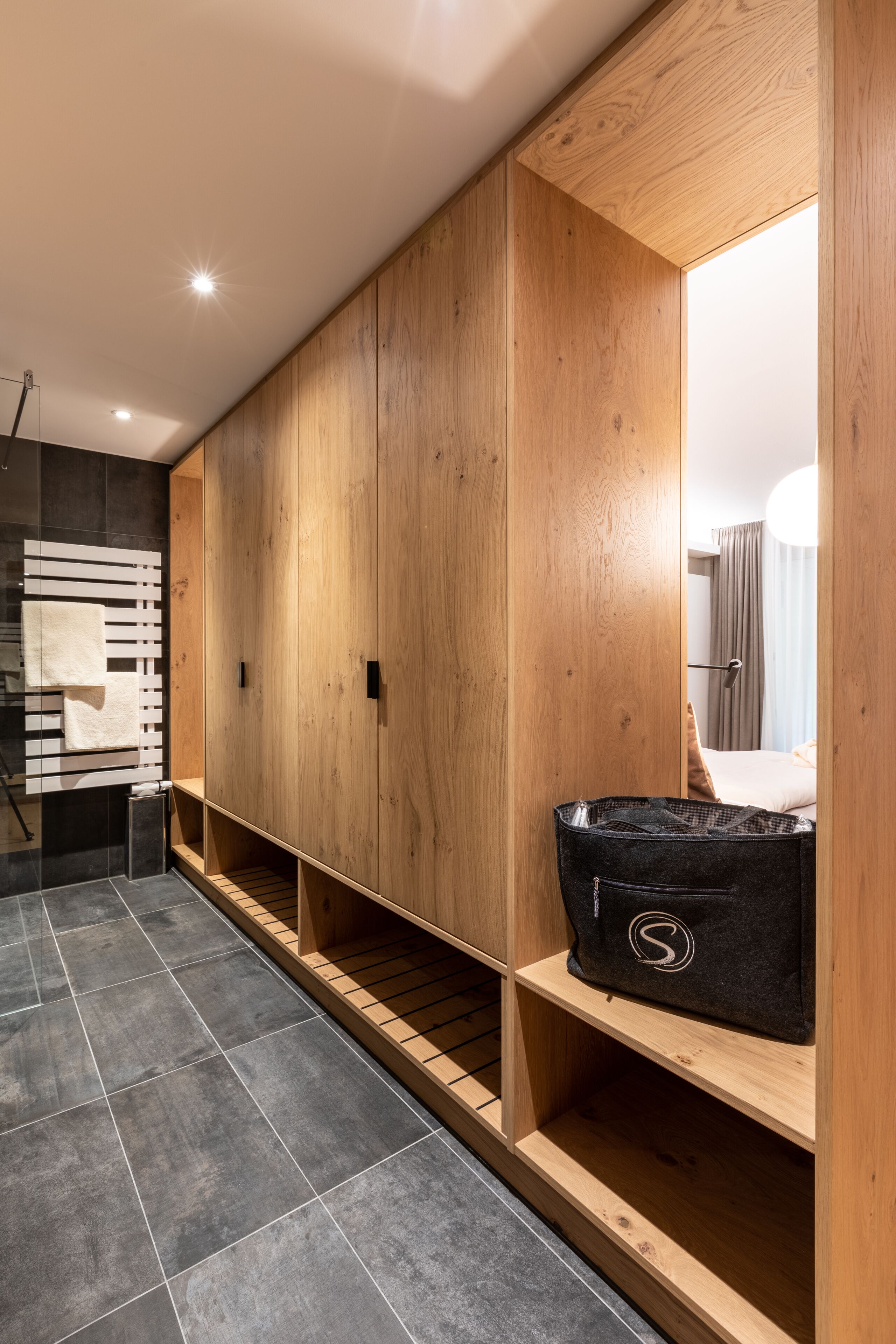 Una habitación de hotel moderna con armario de madera, una maleta negra y suelo de baldosas.