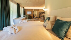 A hotel room with a large bed, a sitting area with a sofa and armchairs, a desk, and a large mirror.