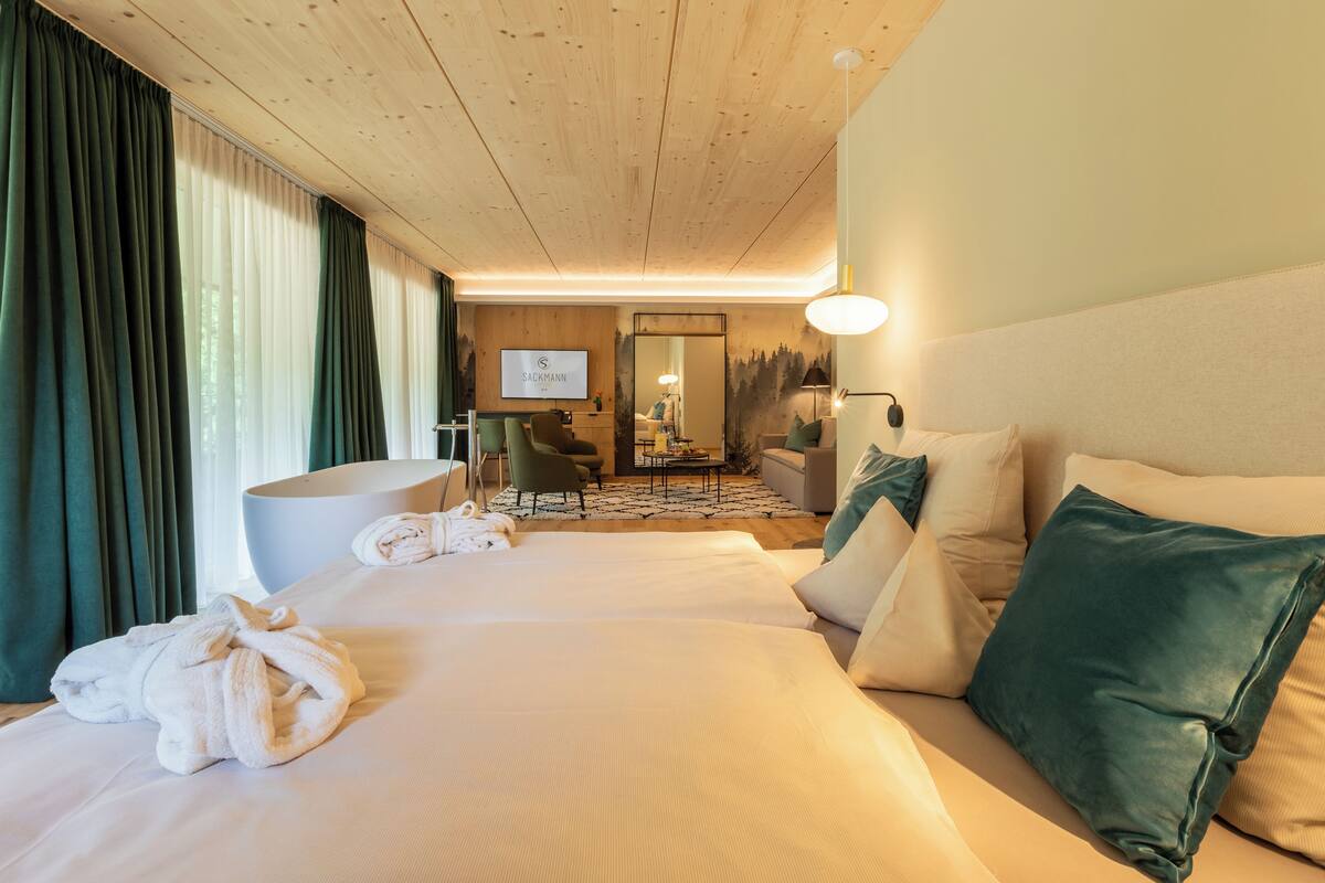 Ein Hotelzimmer mit einem großen Bett, einer Sitzecke inklusive Sofa und Sesseln, einem Schreibtisch und einem großen Spiegel.