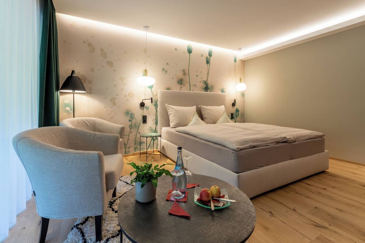 Ein modernes Schlafzimmer mit einer Couch, einem runden Tisch mit einer Pflanze, einer Flasche und Äpfeln.