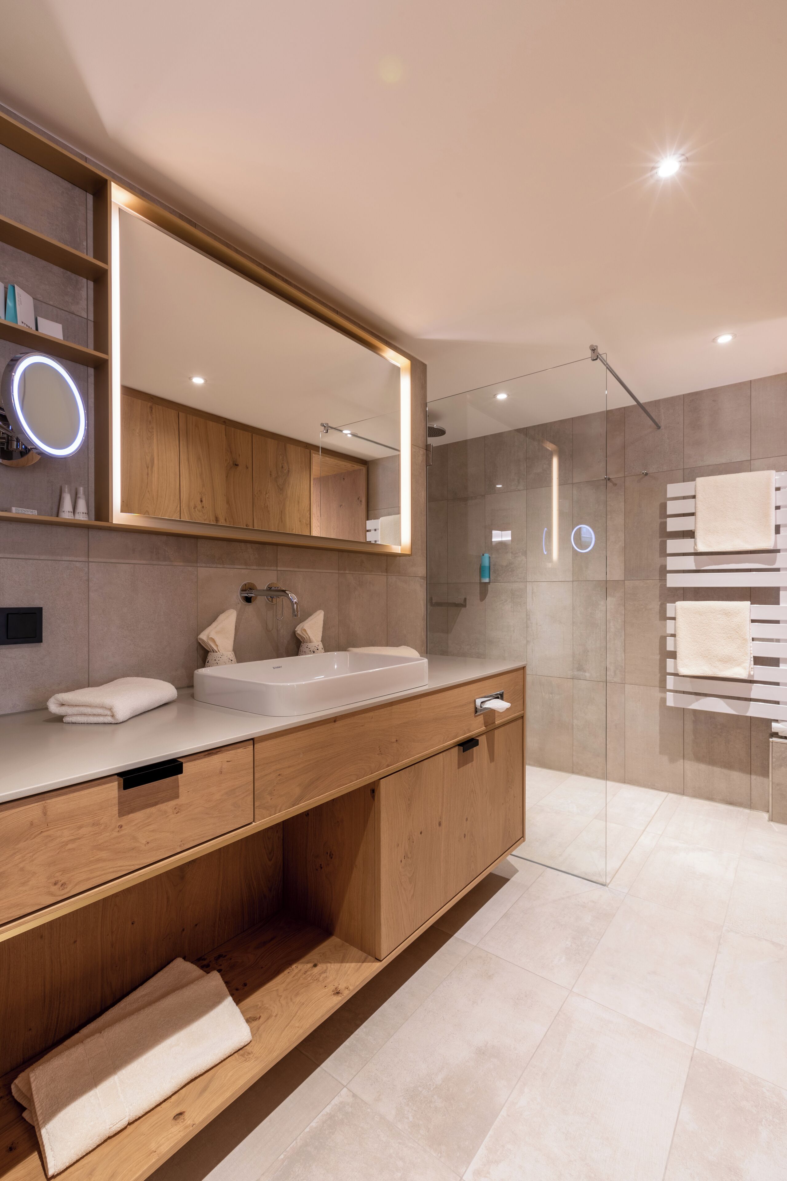 A modern bathroom with a large mirror, wooden vanity, and a glass shower enclosure.