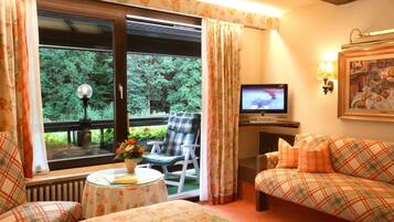 A cozy room with a sofa, a chair, a table with a vase, and a television.