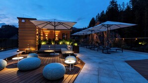 An outdoor patio area with wooden flooring, round seating, and umbrellas.