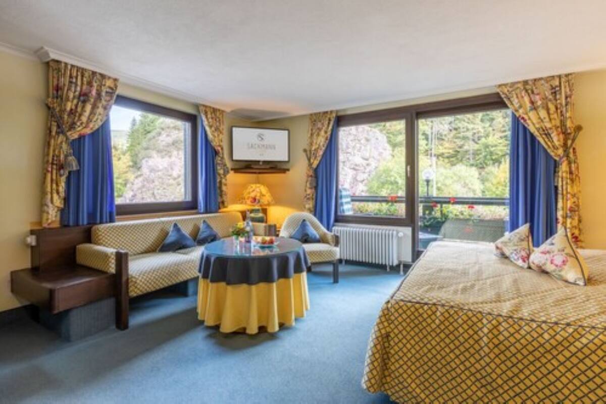 Ein Hotelzimmer mit einer Couch, einem runden Tisch, einem Bett und großen Fenstern mit Vorhängen.