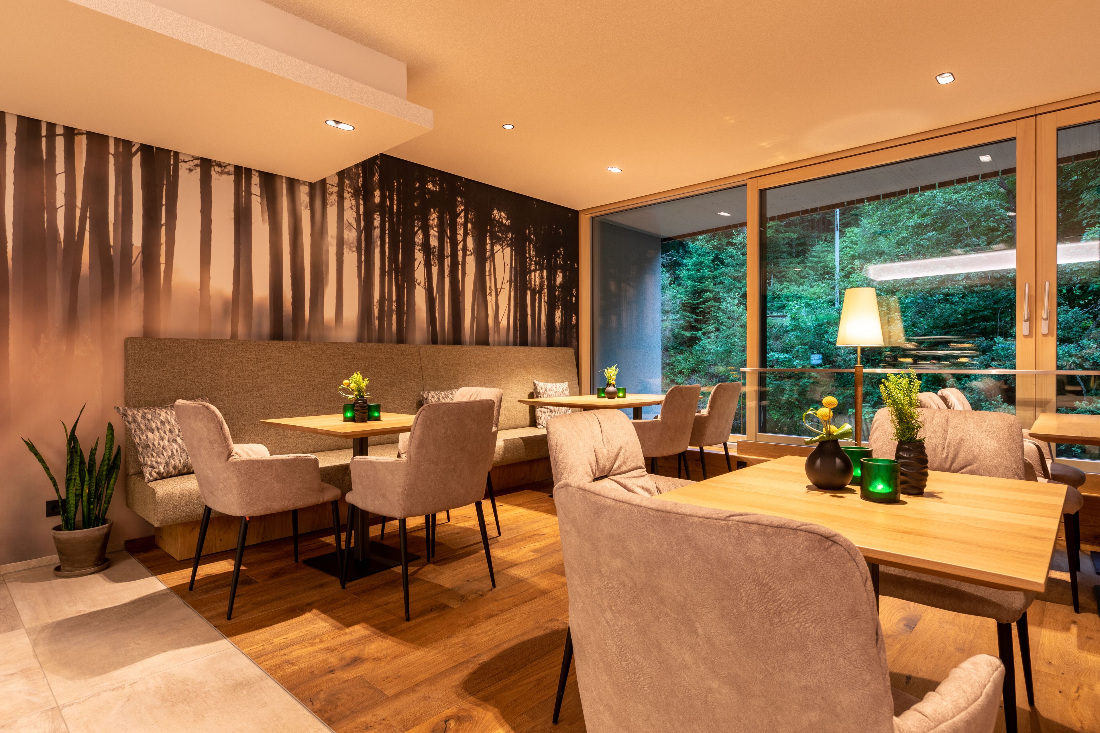 A modern dining area with a wooden table and chairs, a sofa, and a large window with a view of trees.