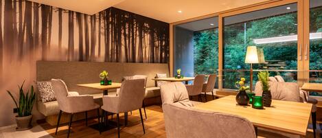 A modern dining area with a wooden table and chairs, a sofa, and a large window with a view of trees.