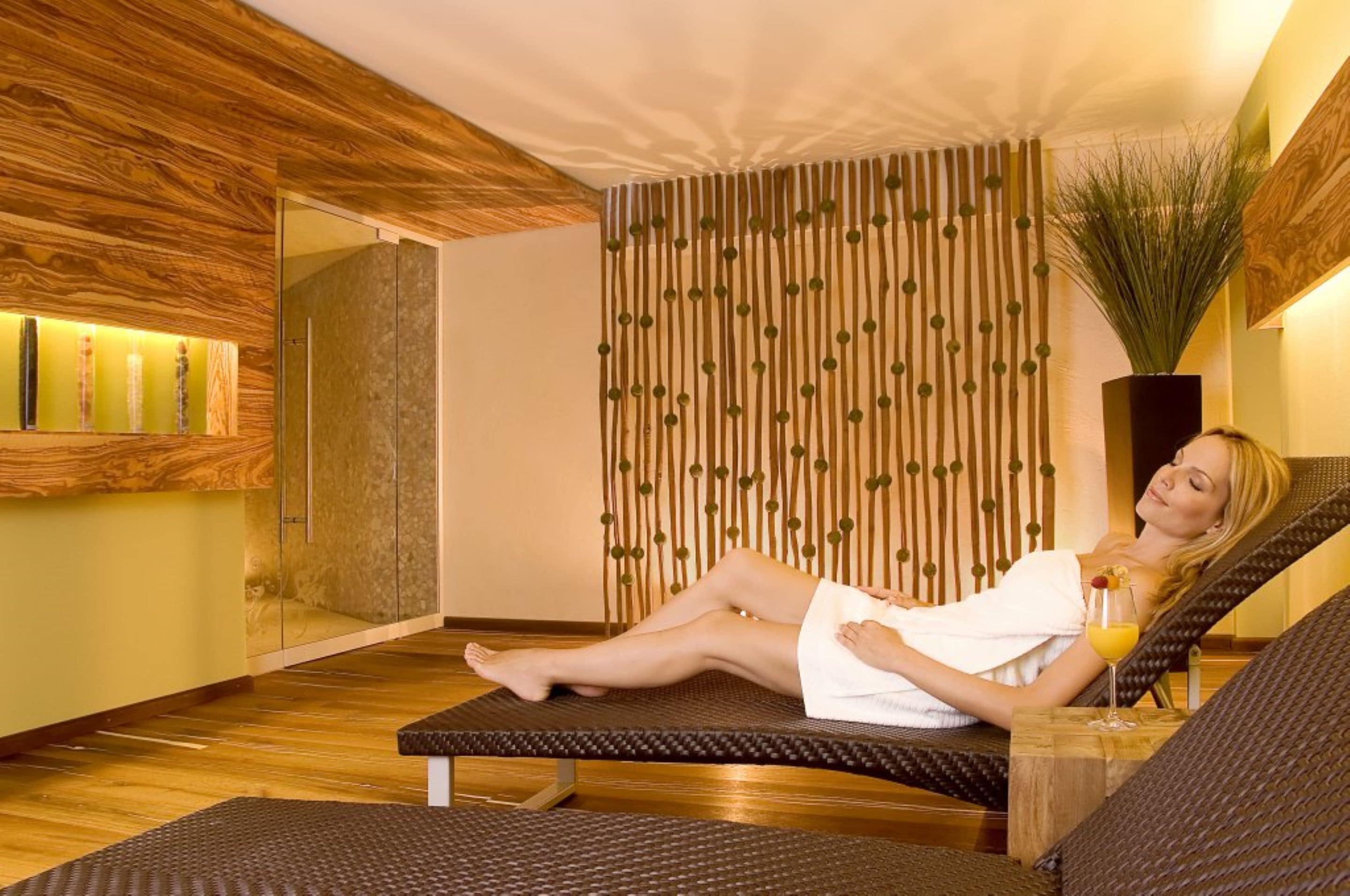 Un cuarto de spa con techo de madera, pared con líneas verticales, una planta grande y una silla reclinable con un vaso de jugo de naranja.