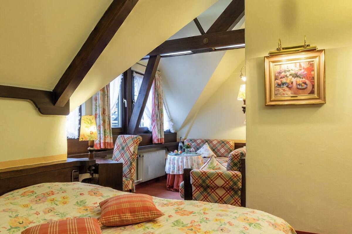 Ein Schlafzimmer mit einem großen Bett, einem Schreibtisch und einem Stuhl. Ein Fenster mit Vorhängen und ein Bild an der Wand sind ebenfalls vorhanden.